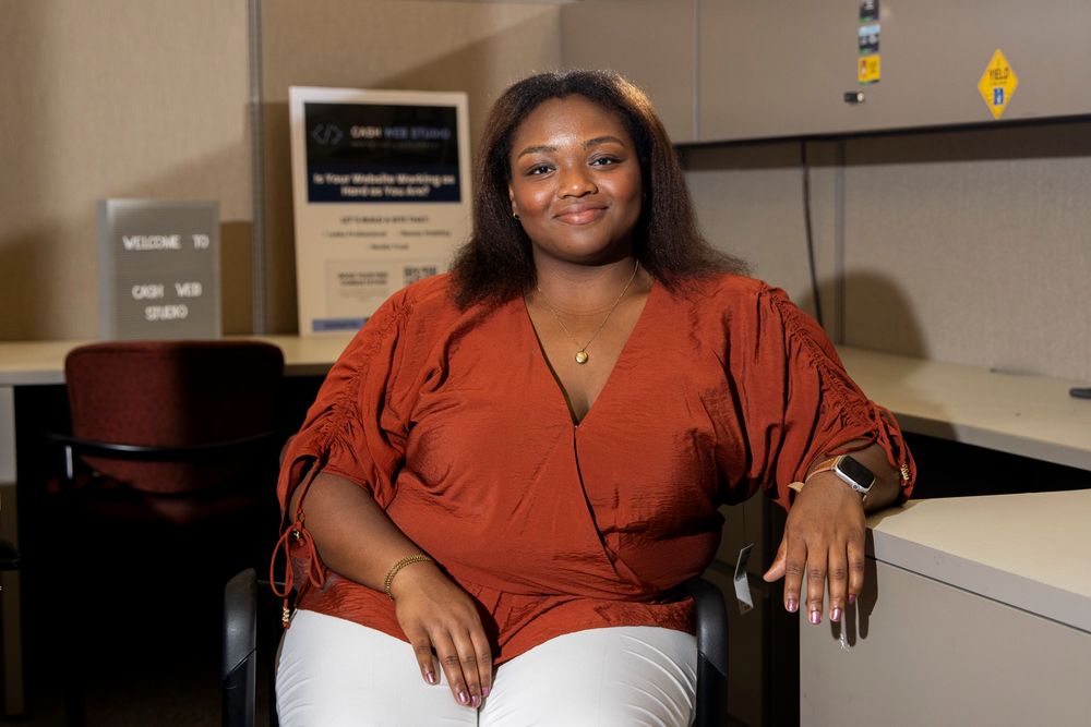Camille Cash smiling at her desk, with a Welcome to Cash Web Studio sign behind her